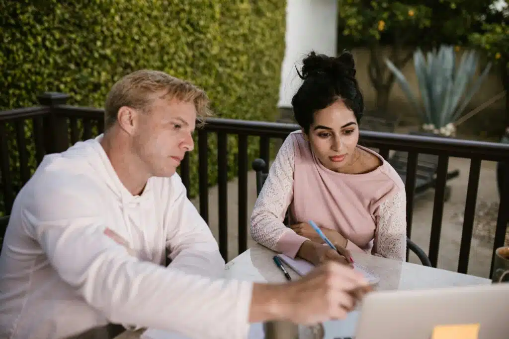 A man and woman engaged in online learning outdoors, collaborating on a laptop.