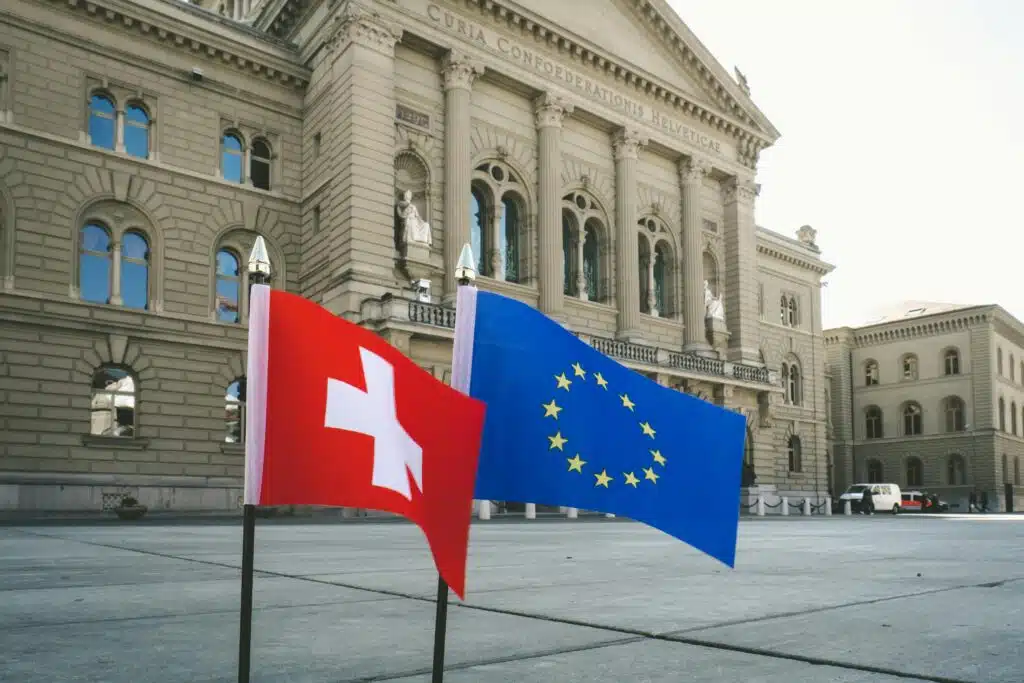 Front view of Swiss Parliament Building in Bern with Swiss and EU flags.
