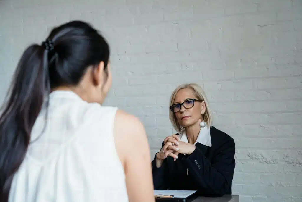 Two women having a serious conversation in an office setting against a brick wall background.